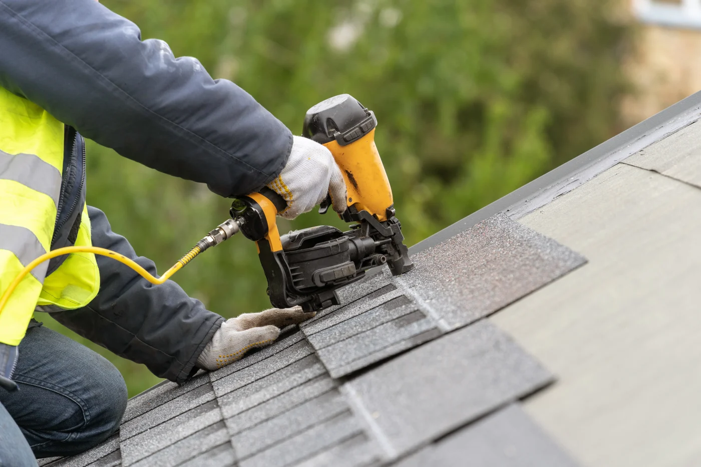 A roof installer places nails into shingles