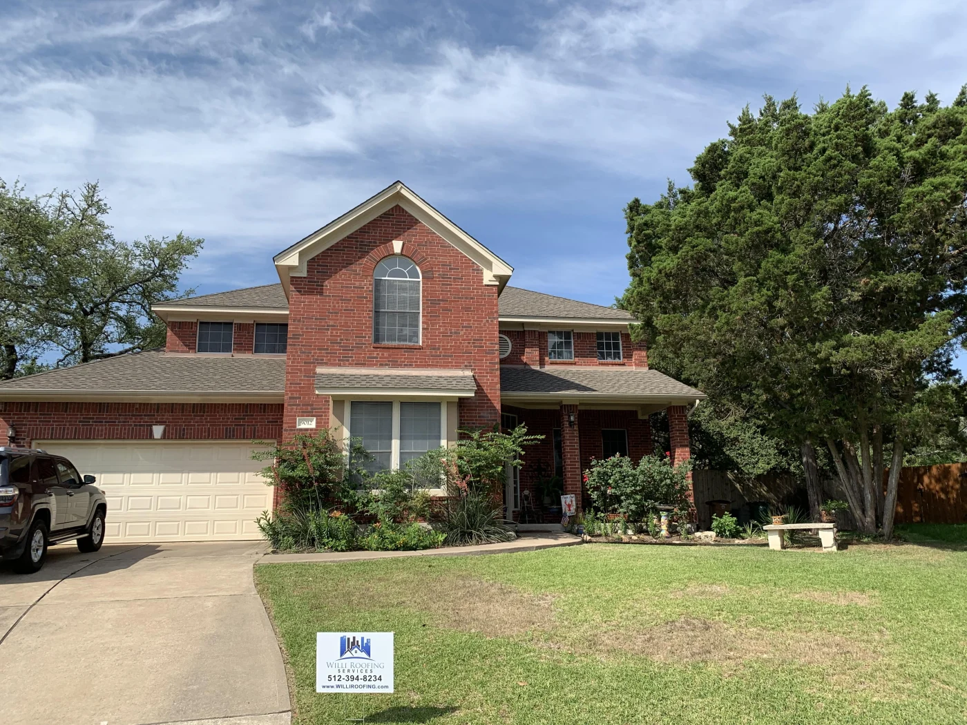 A two-story brick Austin, TX home with a new asphalt shingle roof installed by Willi Roofing