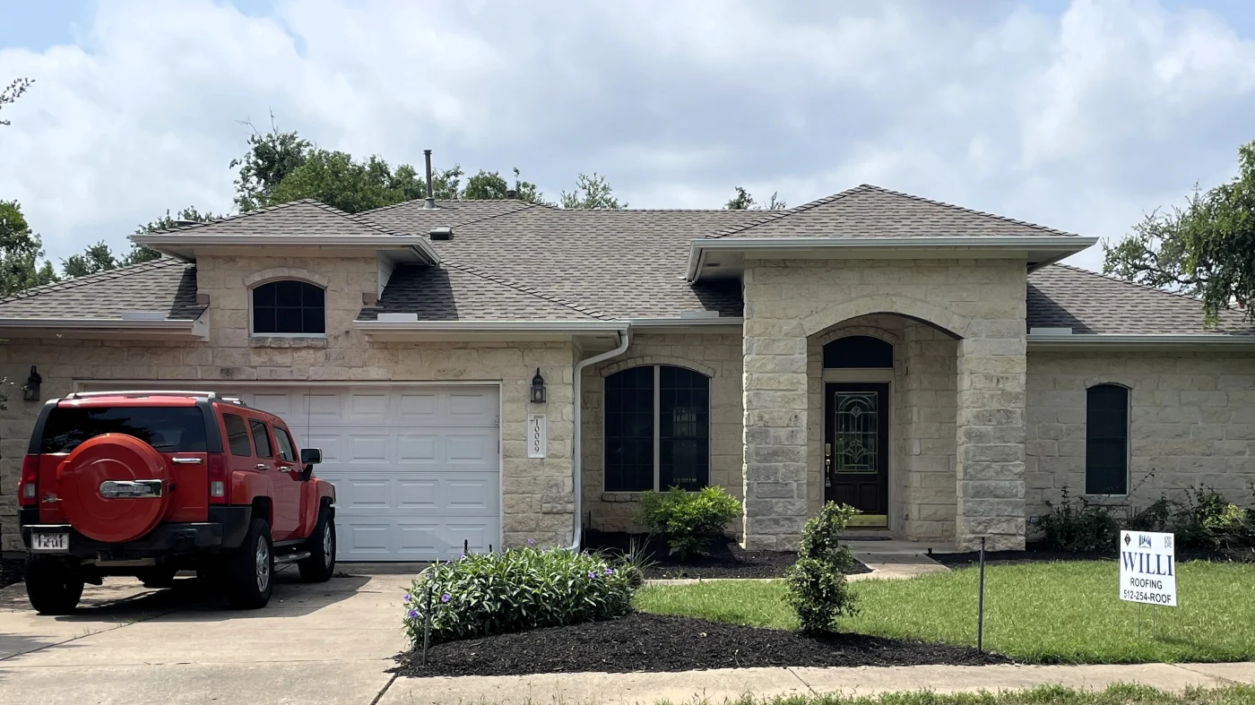 A white brick house with new brown asphalt shingle roofing.