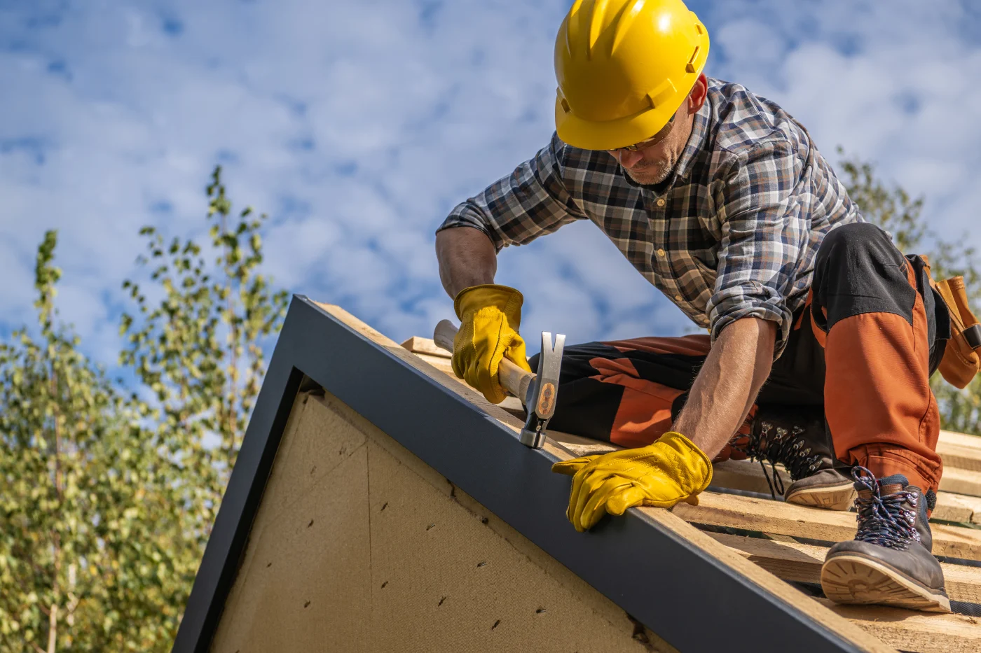 A roofer hammering nails during a roof replacement on a house.