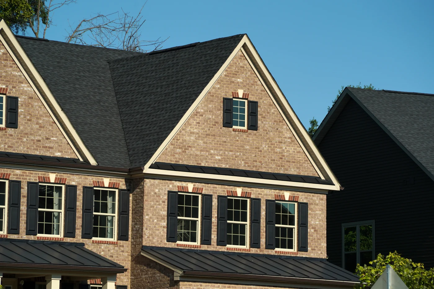 A close-up view of an asphalt shingle roof and a metal roof on a brick house.