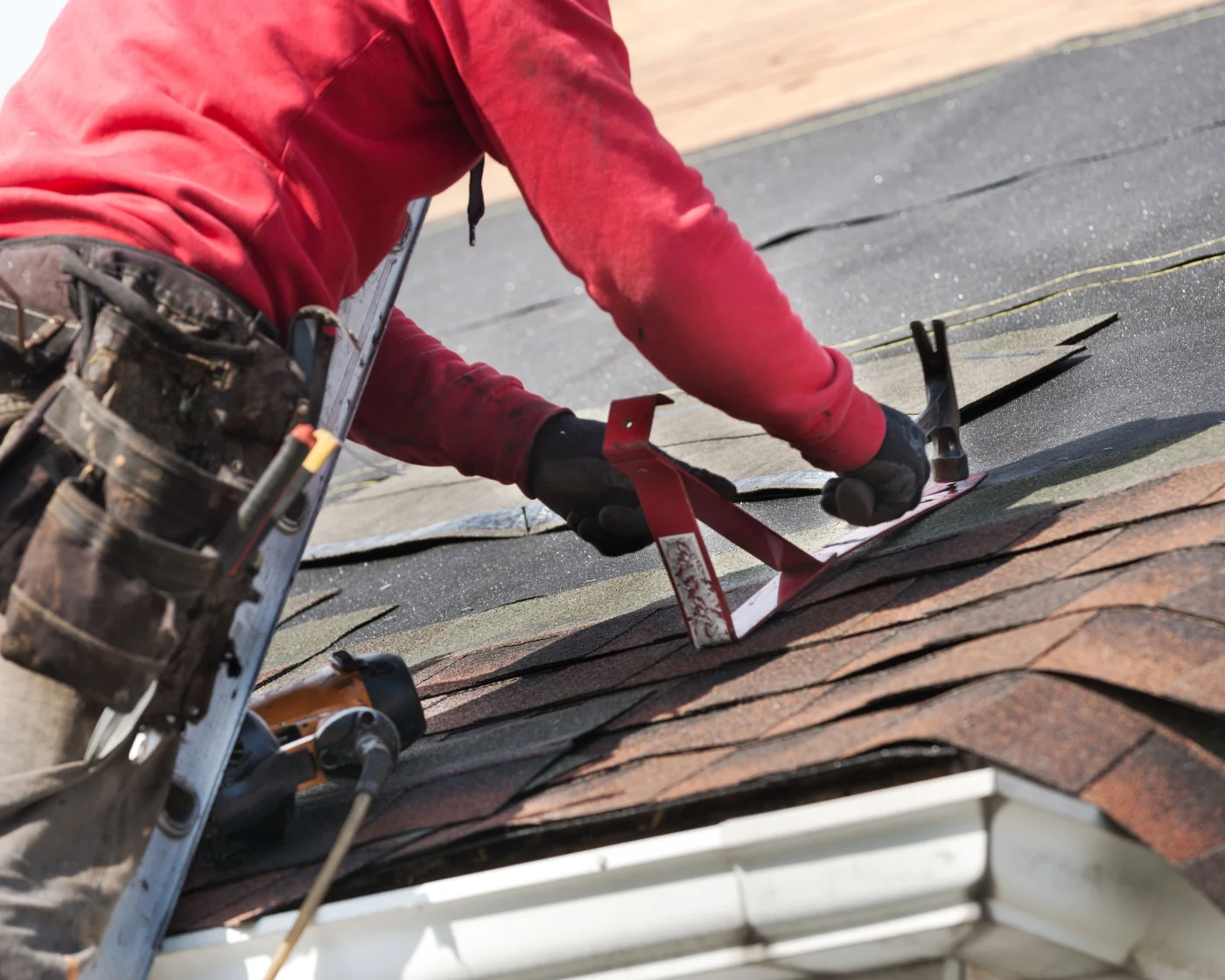 A roofing contractor is hammering new shingles on a house during a roof replacement.