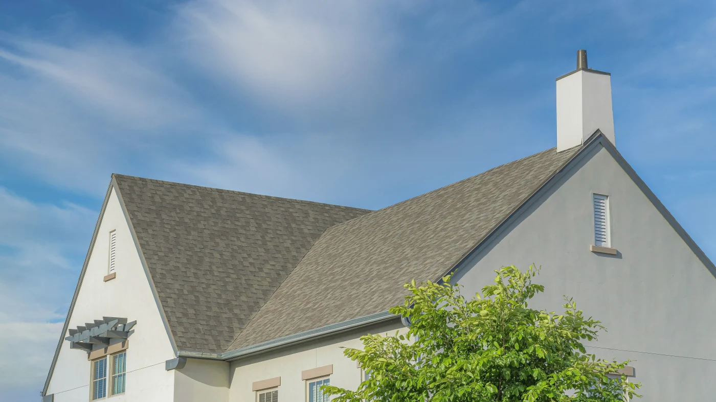 A new asphalt shingle roof  on a two-story building with a tall chimney on top.