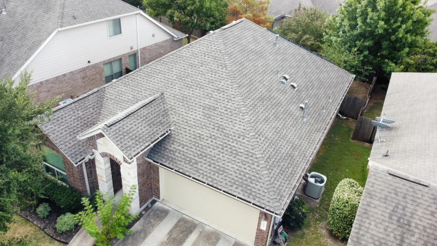 An aerial view of an asphalt shingle roof on a one-story brick house with a tan garage door.