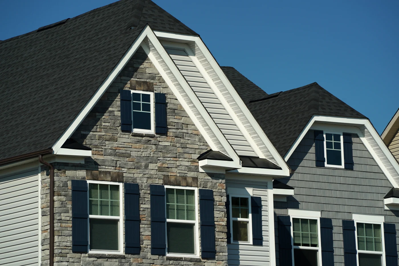 A black asphalt shingle roof on a multi-story house with stone and gray siding.