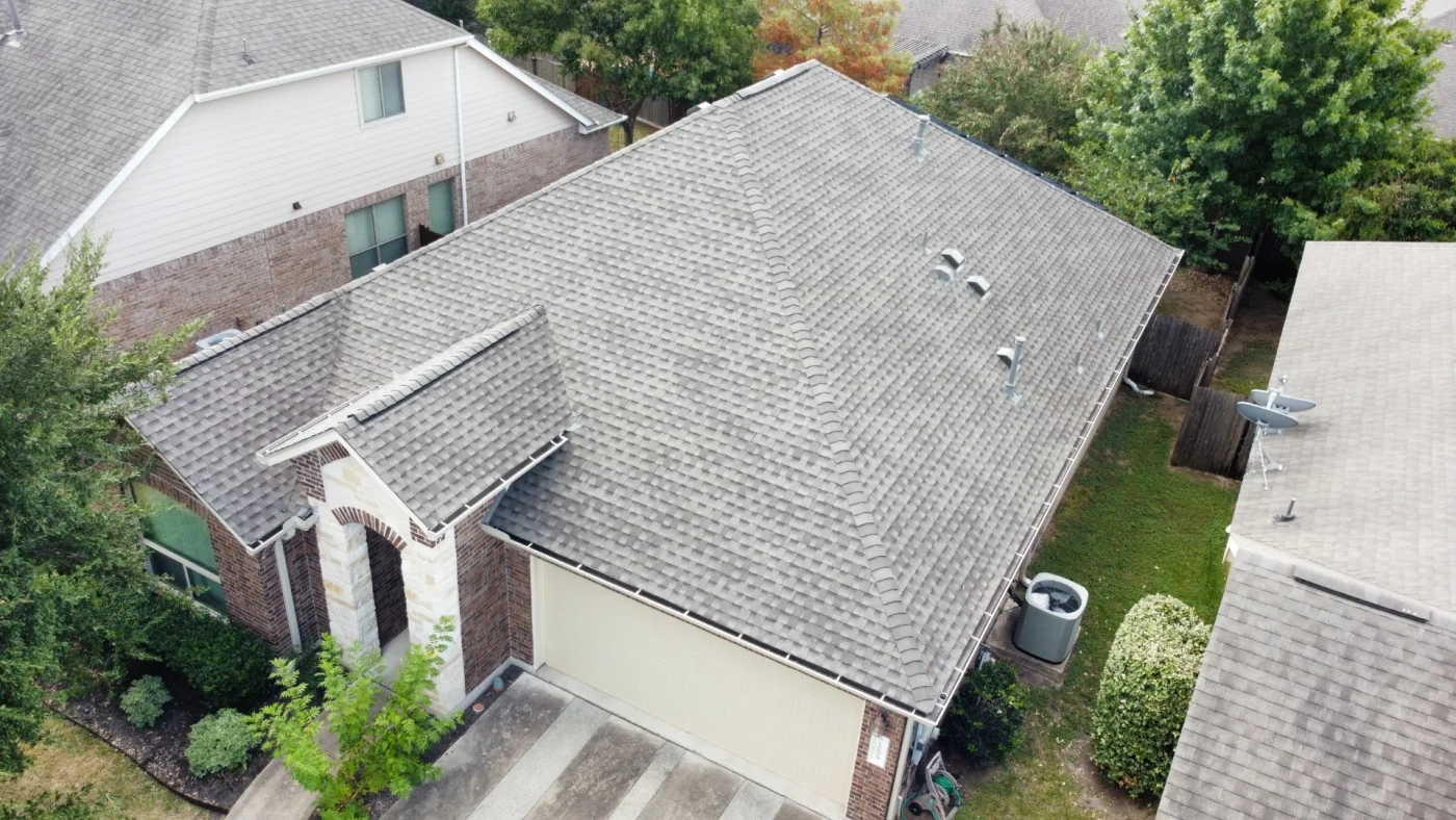 Amazing Roof Replacement | Buda, TX | Willi Roofing Aerial view of a suburban home showing a complete asphalt shingle roof in good condition with ridge vents, plumbing vents, gutters, and a two-car garage.