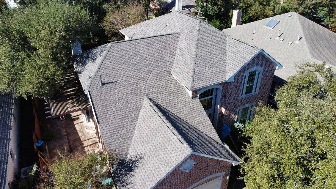 Captivating Roof Replacement | Buda, TX | Universal Roof An aerial view of a large two-story brick home, showcasing a replaced gray asphalt shingle roof with multiple ridges and valleys surrounded by mature trees.