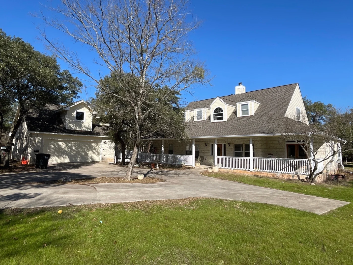 Large two-story home with light stone and beige siding exterior featuring a steep dark brown asphalt shingle roof.