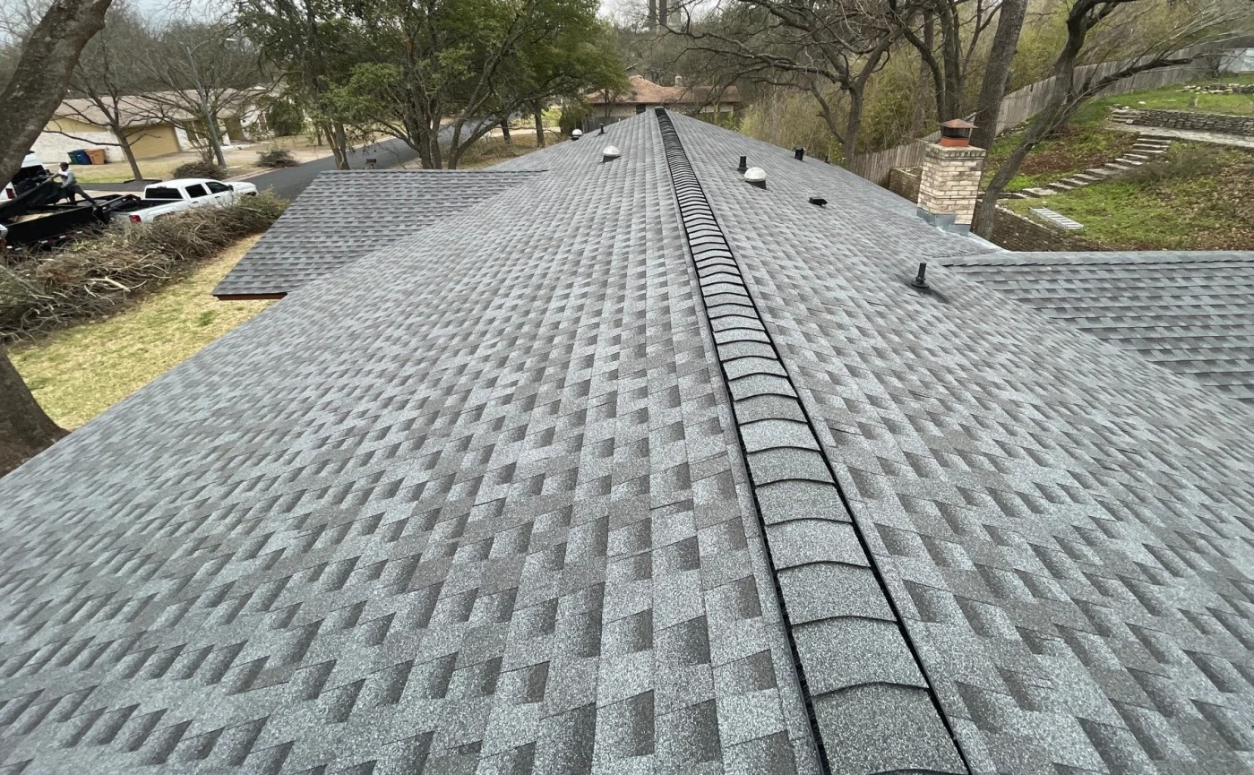 Close-up view of a newly installed gray asphalt shingle roof with ridge vents and several vent pipes evenly spaced along the peak.