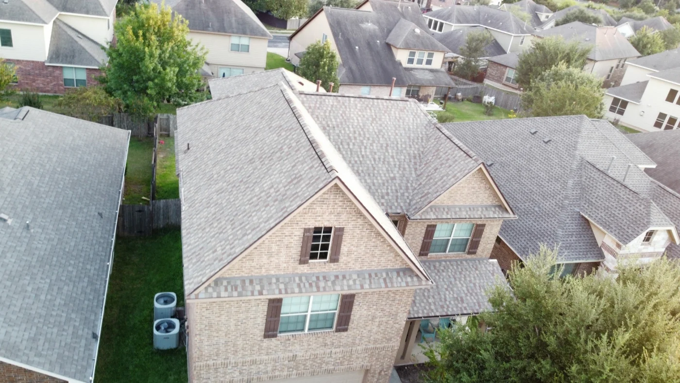 Aerial view of a two-story brick home with a newly installed asphalt shingle roof in Bee Cave, TX.