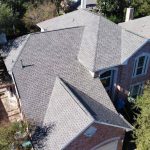 Aerial view of a two-story brick home with a newly installed asphalt shingle roof in Kyle, TX