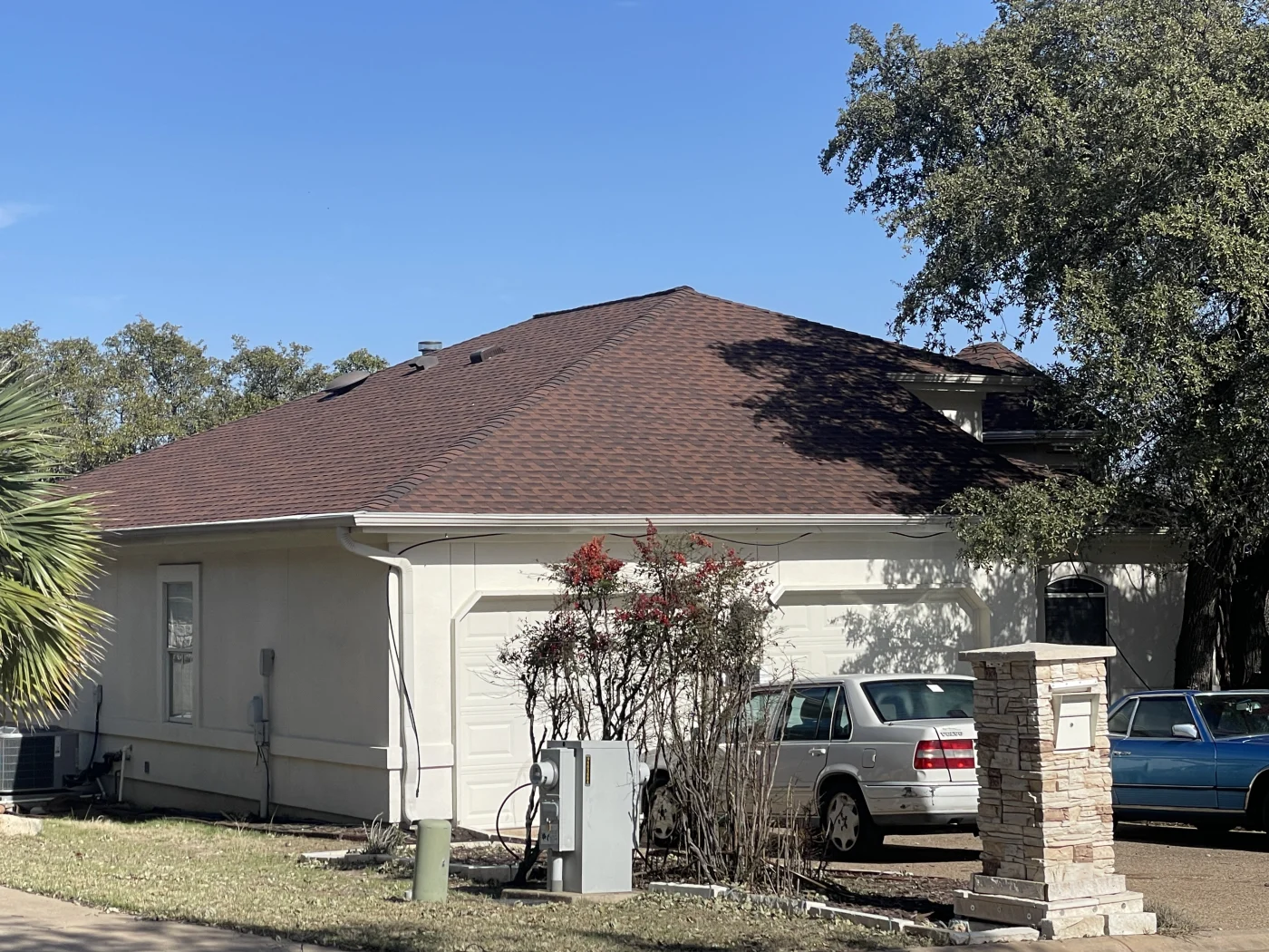 Side view of a residential home with a newly installed asphalt shingle roof replacement, showcasing a rich brown shingle color and clean roof edges.