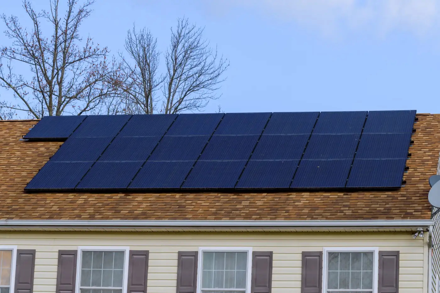 A home with yellow siding, gray shingle roofing, and solar panels.