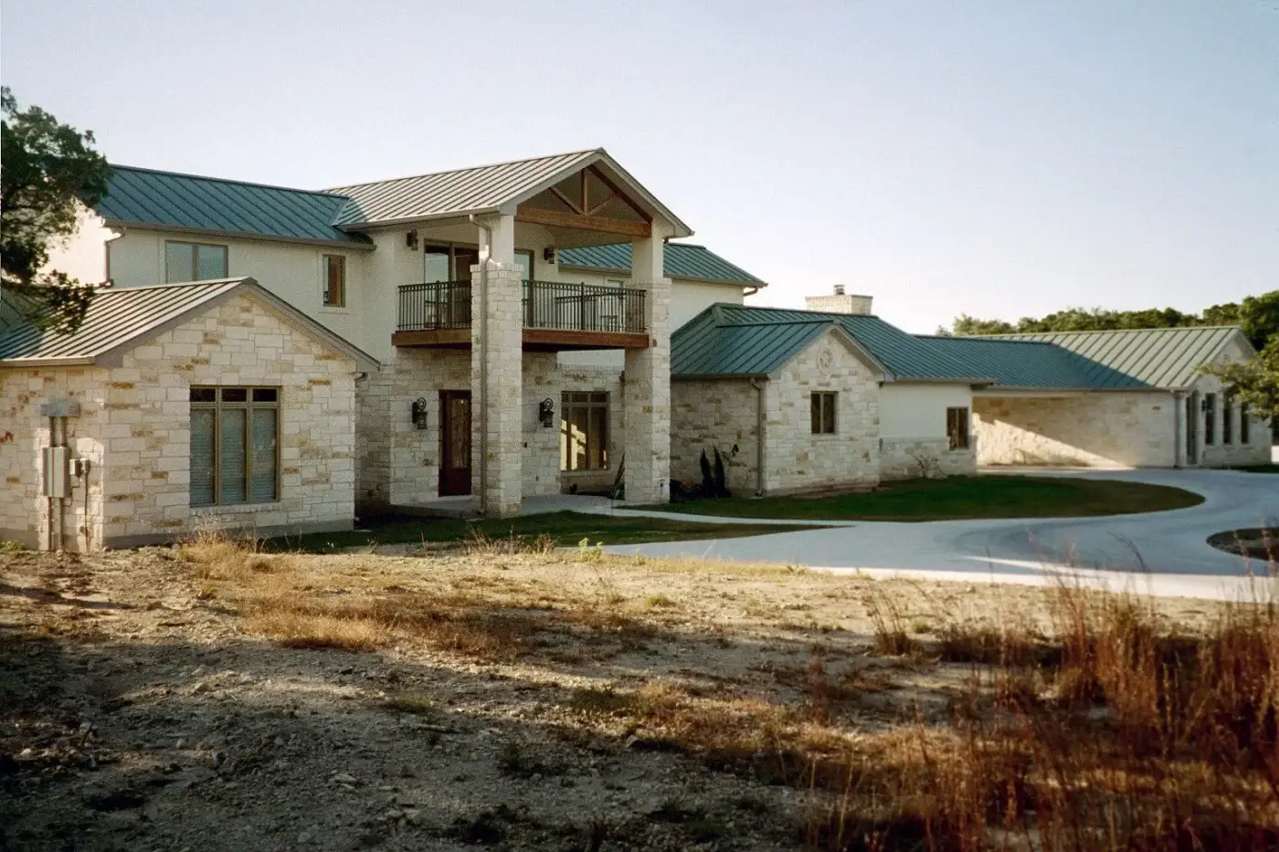 A two-story farmhouse with a white metal roof and light stone exterior.