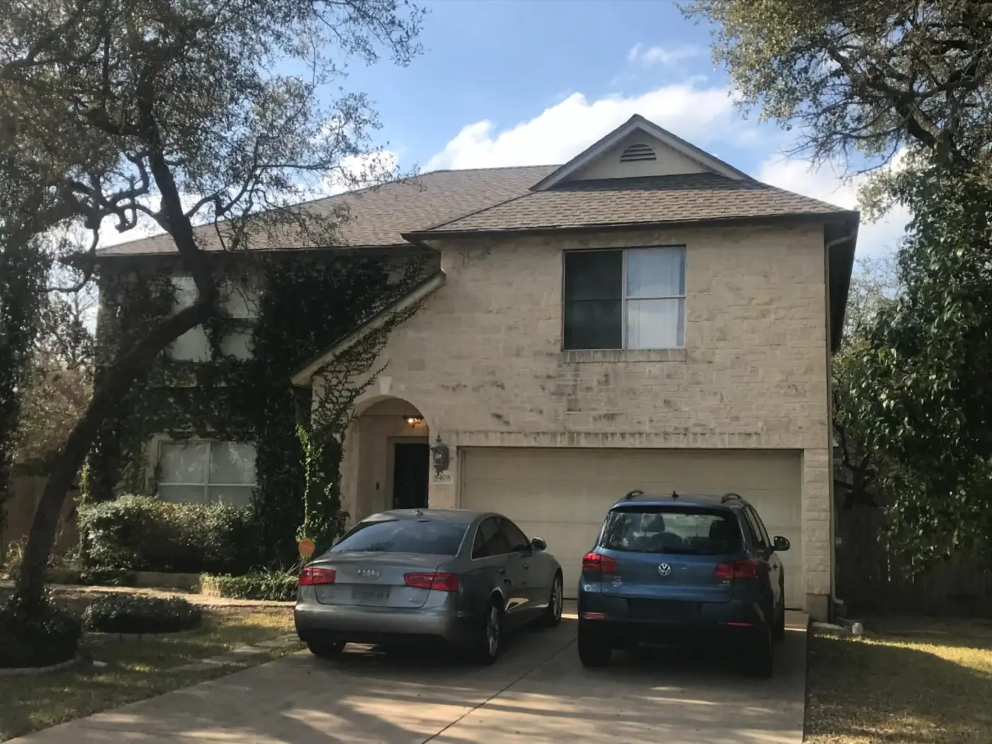 An aerial view of a two-story brick home with a newly installed light gray asphalt shingle roof.
