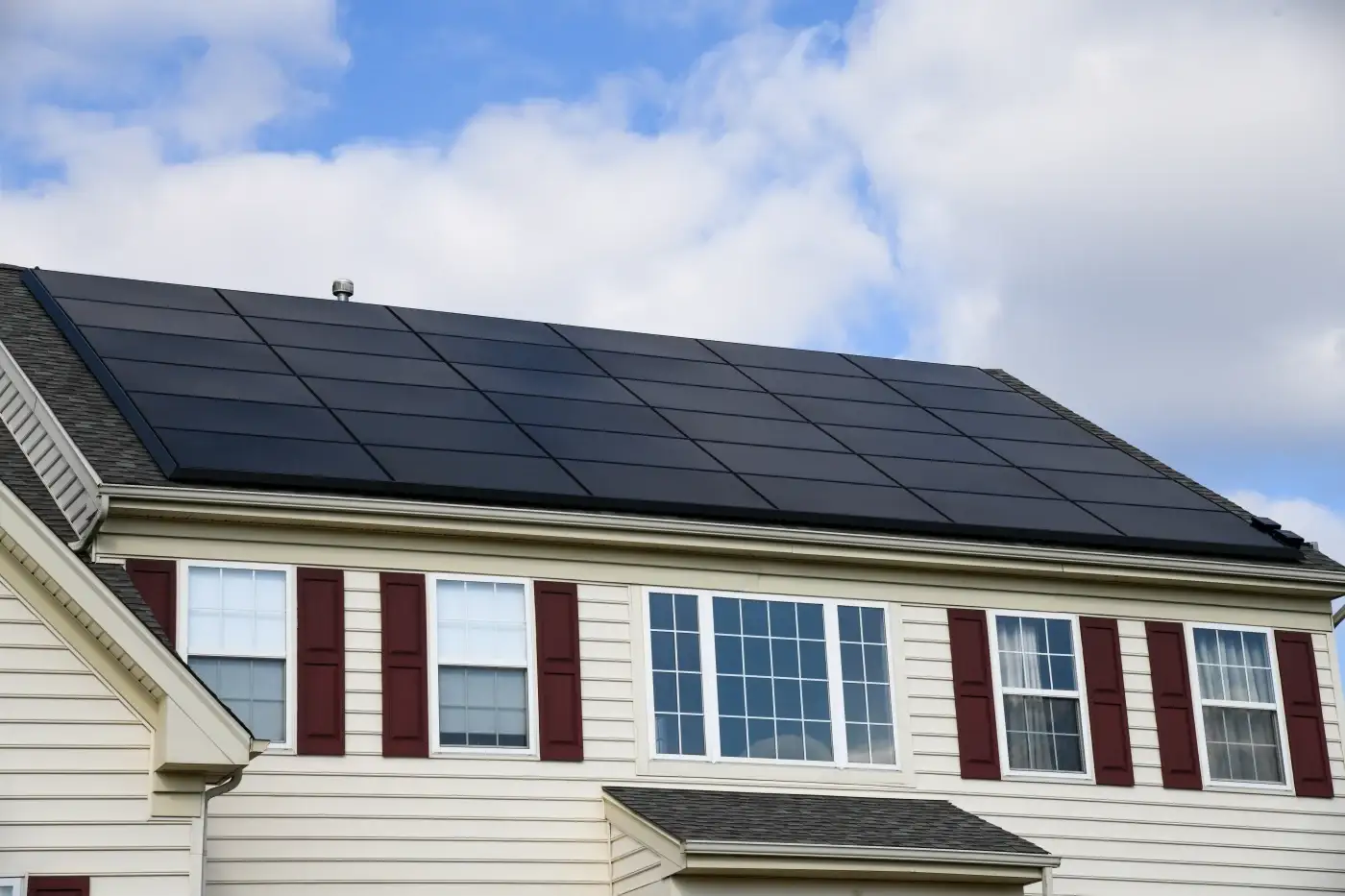 Front view of a two-story tan home with solar roofing.