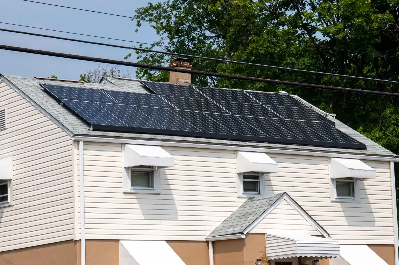 A tan two-story home with multiple solar panels installed across its tiled roof.