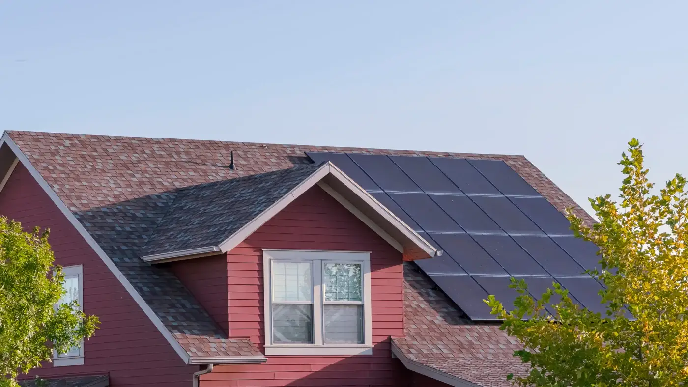 Angled view of a home with red siding, a shingle roof, and solar panels.