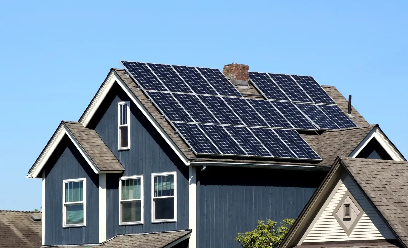 A large two-story home with multiple rows of solar panels installed on the shingle roof.