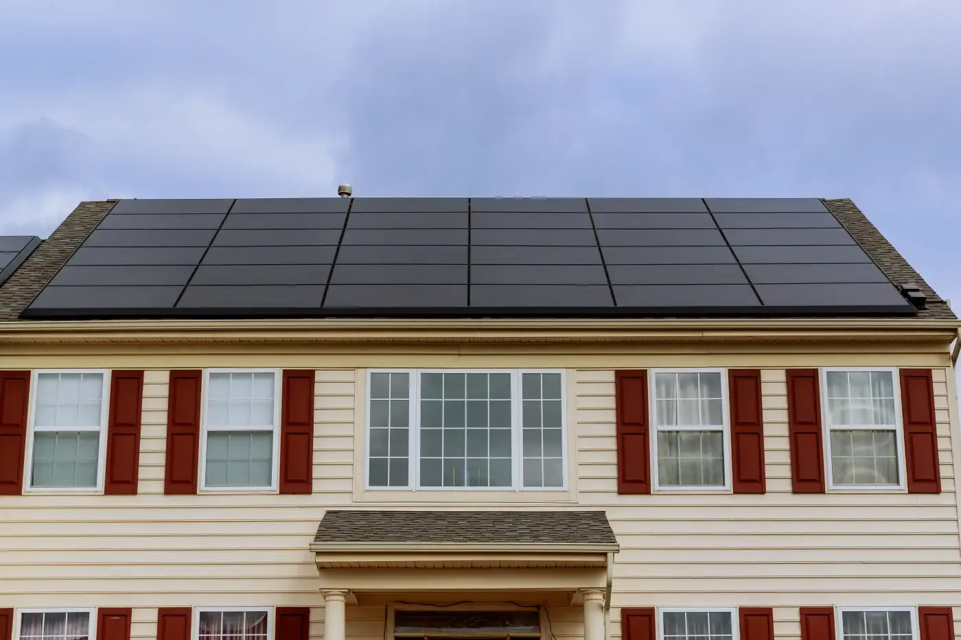 A tan-sided home with white trim and solar panels on the roof.